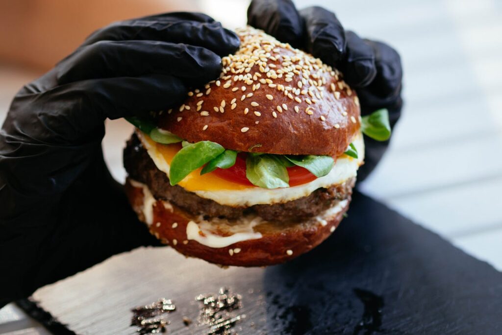 Person nutzt schwarze Handschuhe und hält einen Burger in den Händen httpswww.pexels.comde-defotoperson-die-burger-halt-1251197